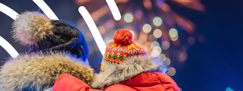 Dad and young boy watching fireworks dressed in coats hats and scarfs.